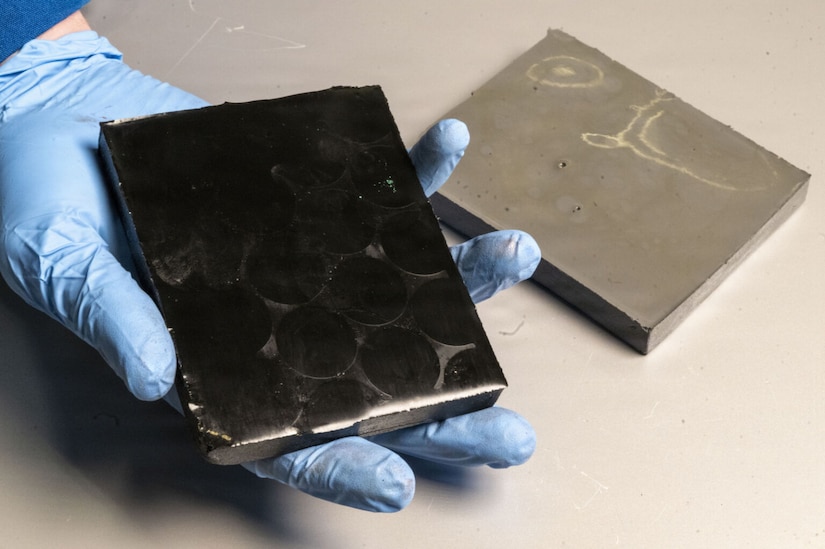 A person holds a black block in a gloved hand. A gray block is on a table nearby.