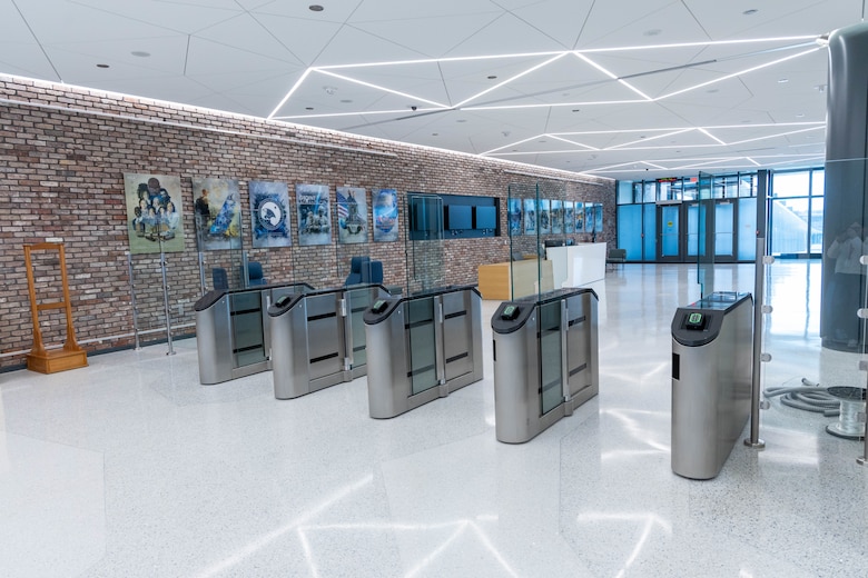 A red brick wall is on the left side with photos hanging on it and grey security columns sit in the middle with a white floor.