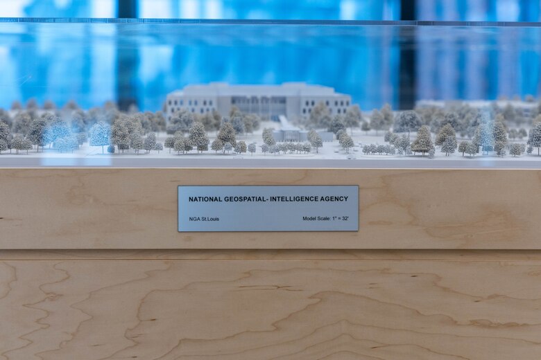 A small grey replica building with grey miniature plants sits in a glass box.