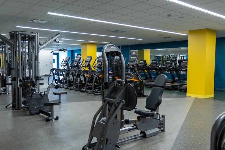 Gym equipment sits in a room with yellow columns, blue walls and grey floors.