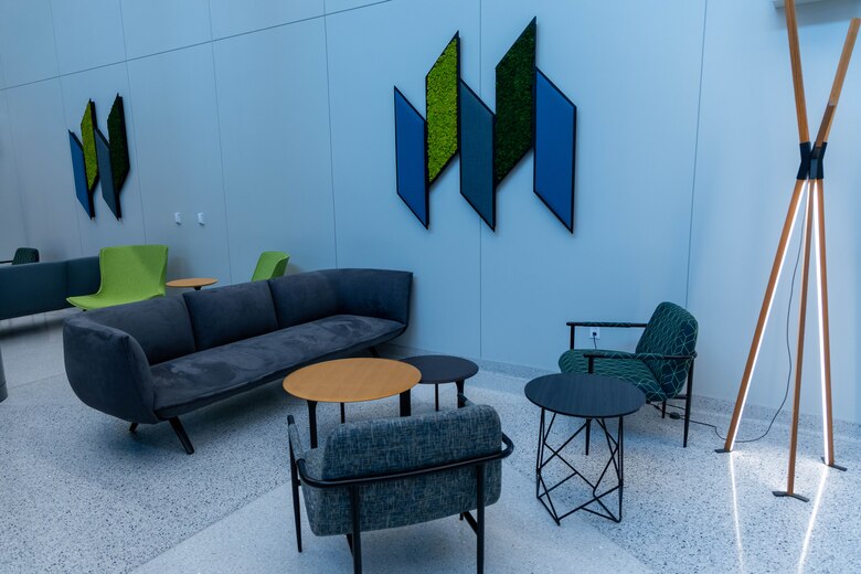 A sitting area with a grey couch, a tan coffee table, and two grey chairs with green and blue artwork on the wall.