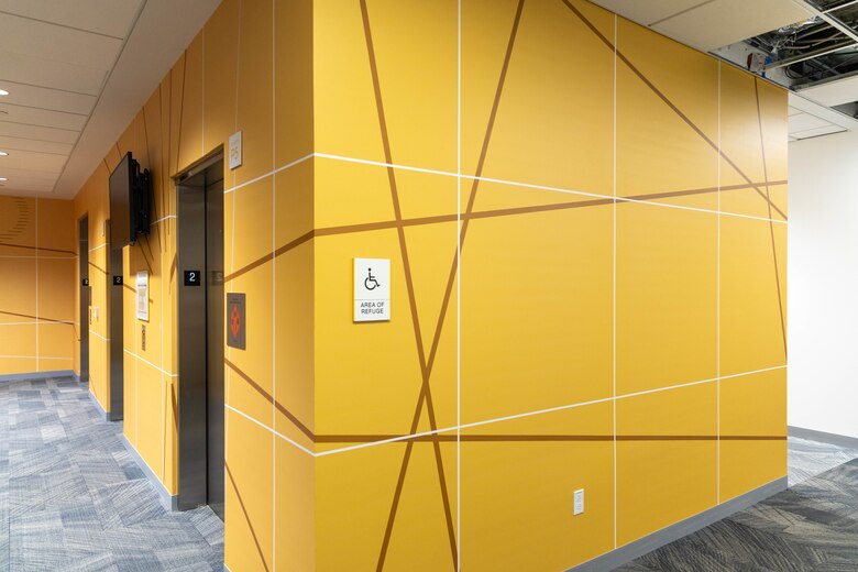 A elevator bank with yellow walls and grey carpet.