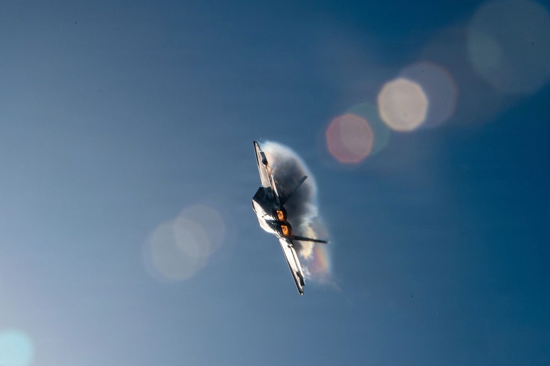 An aircraft flies diagonally into a blue sky in between glare bubbles on its left and right.