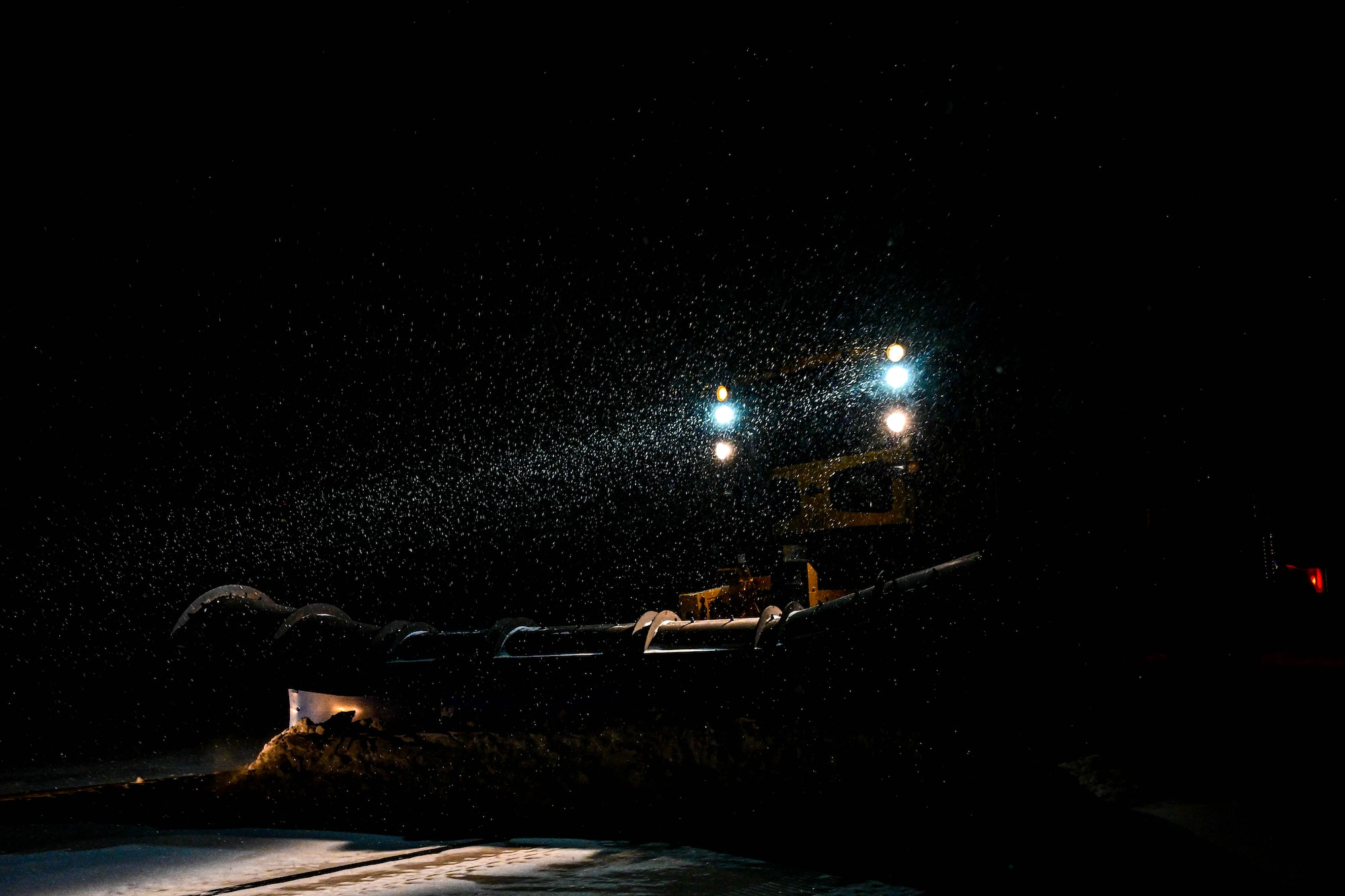 Giant yellow vehicle pushing snow out of the way during the night with very minimal visible light