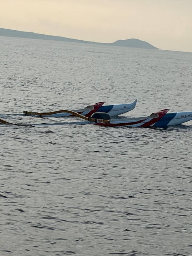 The backend of an outrigger canoe sticks out the top of the water. Partially submerged, a grey hazy sky liters the background.