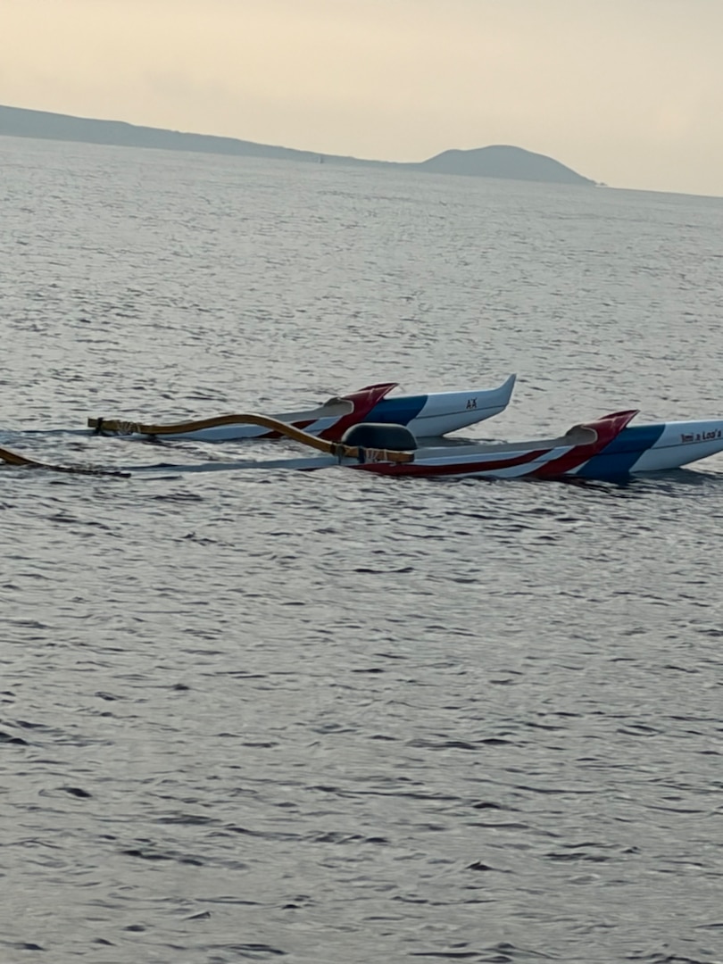 The backend of an outrigger canoe sticks out the top of the water. Partially submerged, a grey hazy sky liters the background.