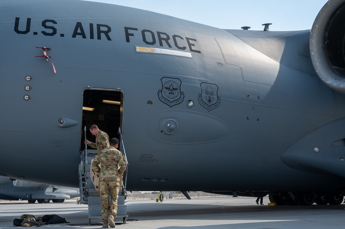 Two Airmen carry a container up the steps onto a C-17 aircraft