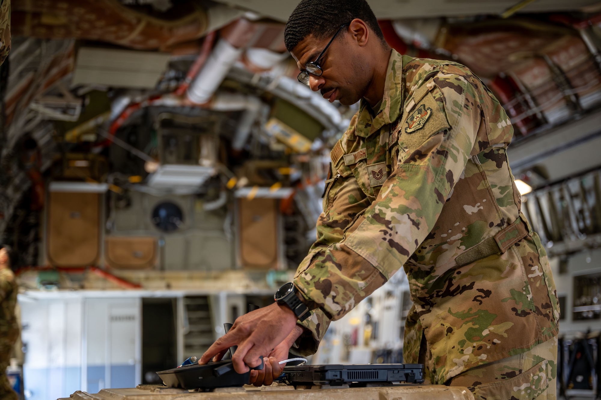 An Airman plugs connects a cable from a laptop into a router inside of a C-17