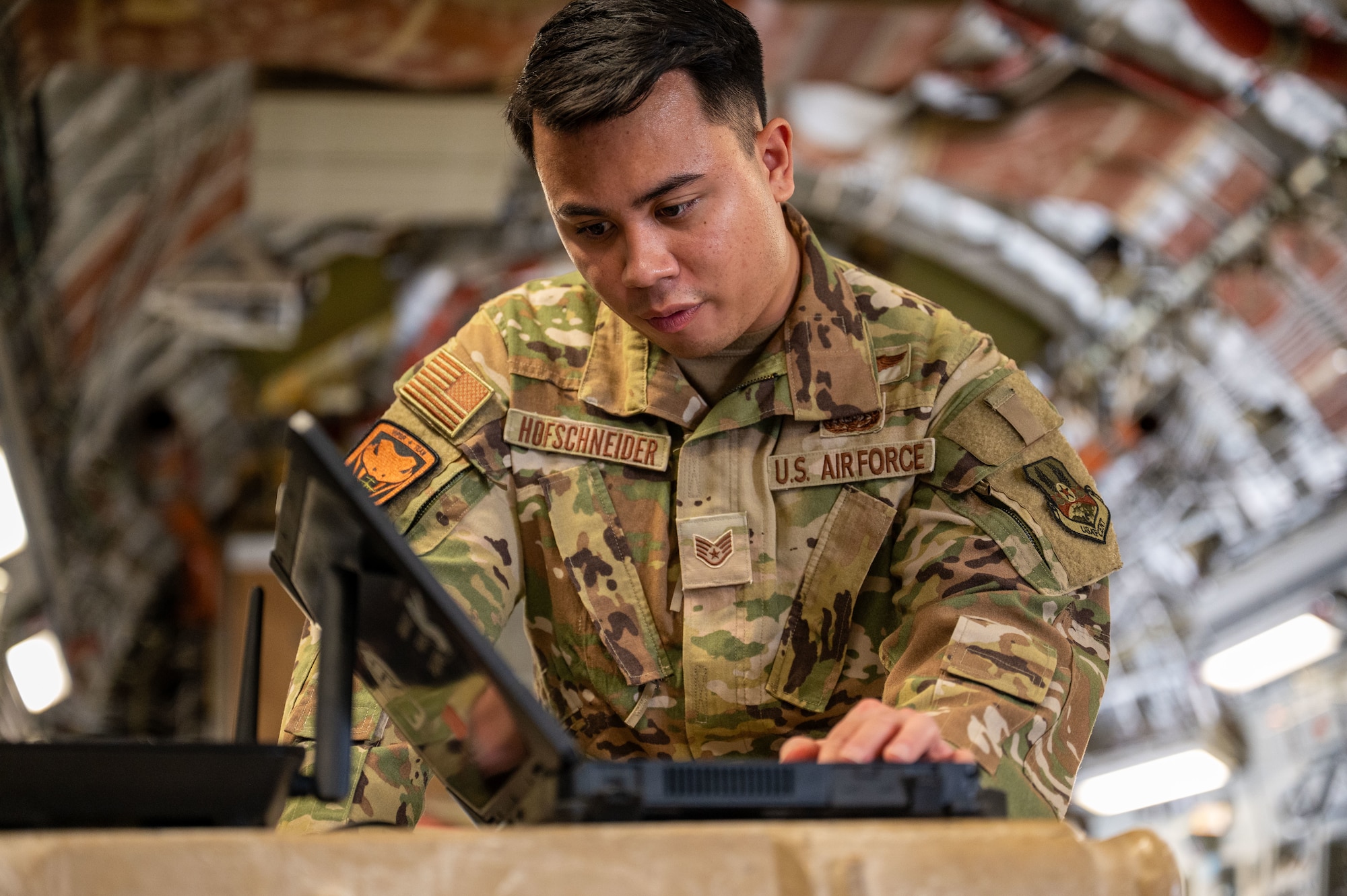 An Airman looks down at a laptop screen from the side inside a C-17