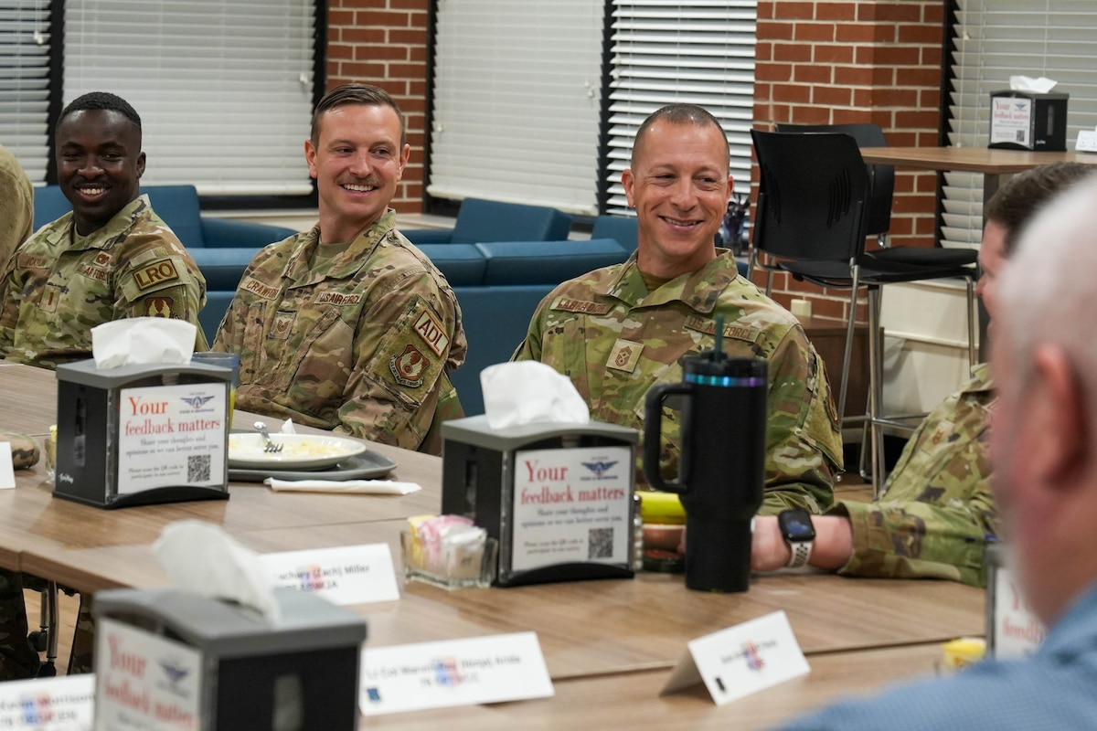 Photo shows group of uniformed individuals sitting at table speaking.