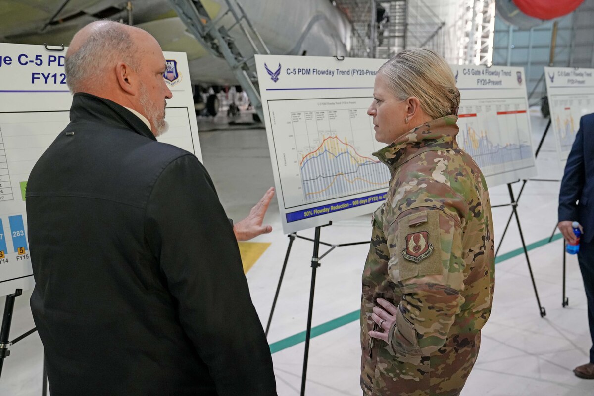 Photo shows two people speaking in front of easel.