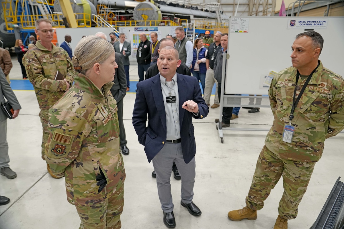 Photo shows group of people speaking inside aircraft hangar.