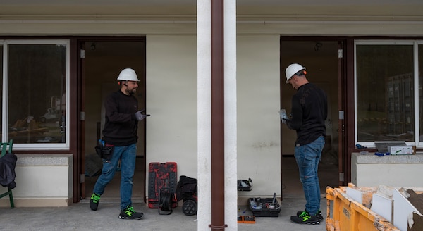 Two Spanish contractors conduct construction works with a white wall in the center.