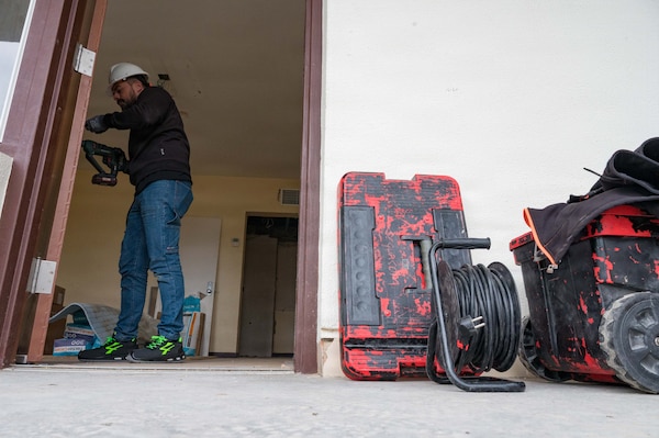 A Spanish contractor works with a drill on a doorjamb with tools to the right side of the photo.
