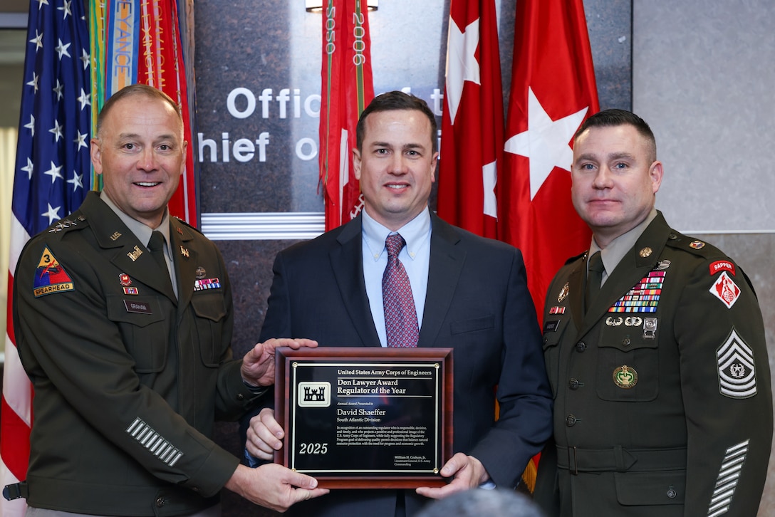 Two soldiers present a man with a plaque.