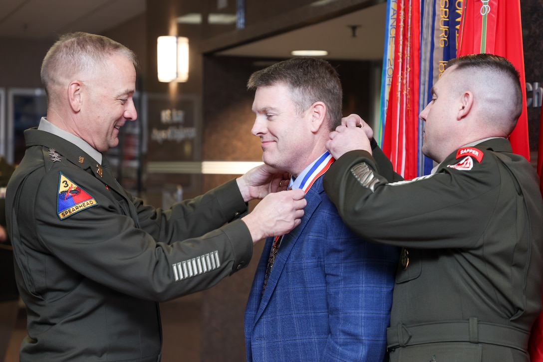 Two Soldiers place a medal around a gentlemen's neck.