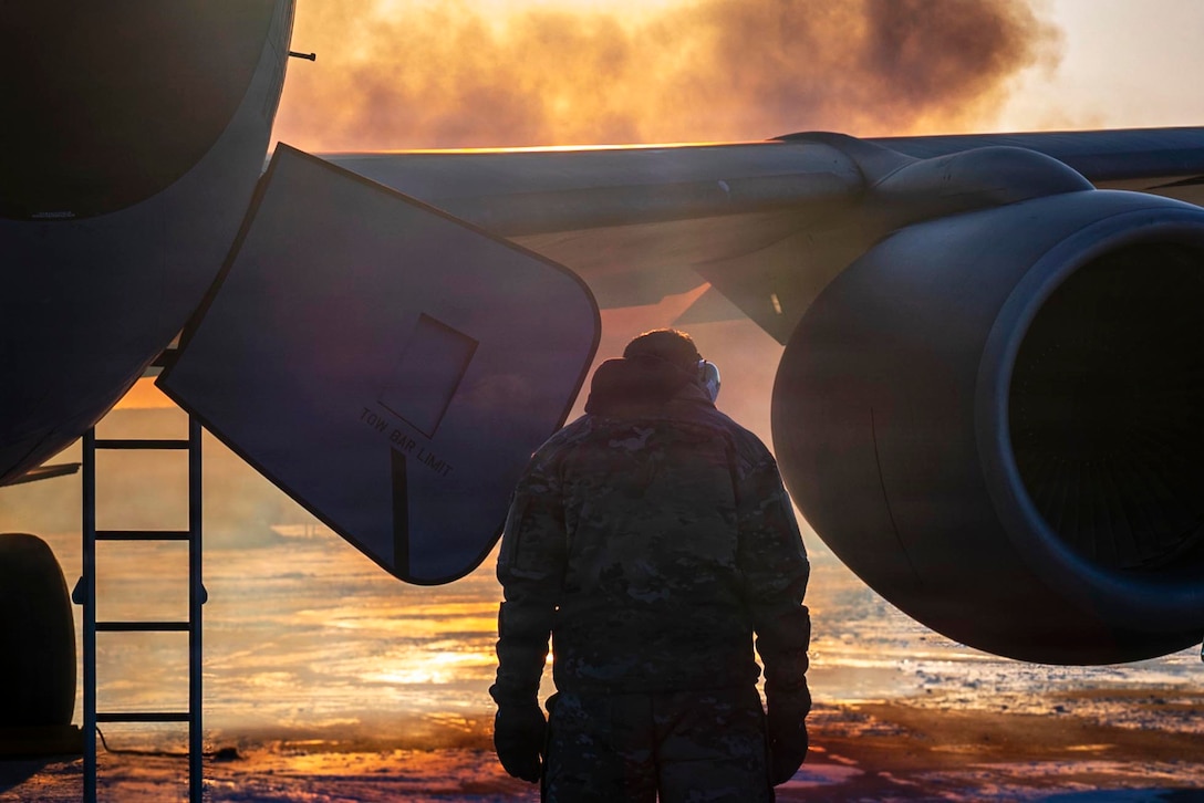 A silhouette of a man holding his head down as he walks toward an airplane wing with dark black and yellow smoke in the background.