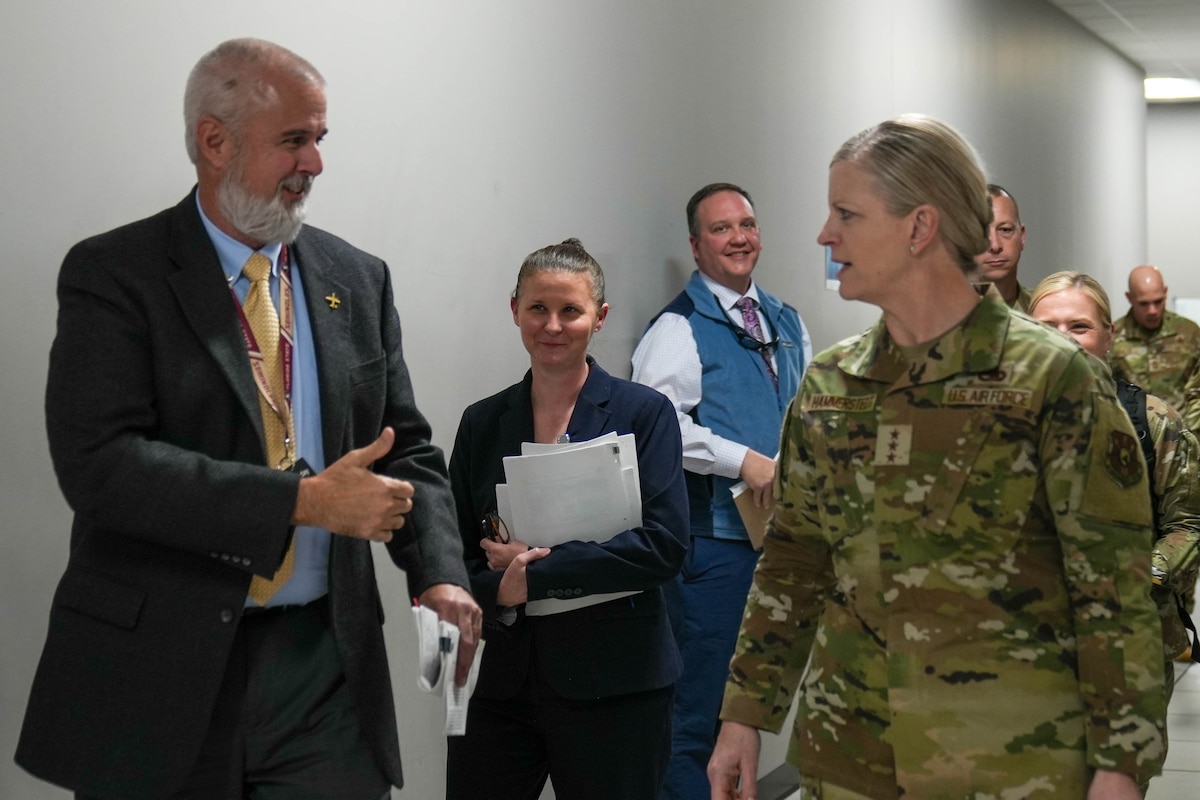 Photo shows group of people speaking while walking down hallway.