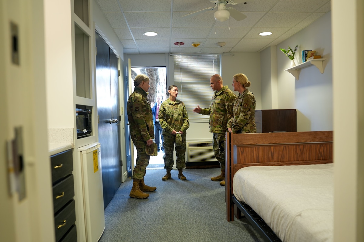 Photo shows group of uniformed individuals speaking inside dorm room.