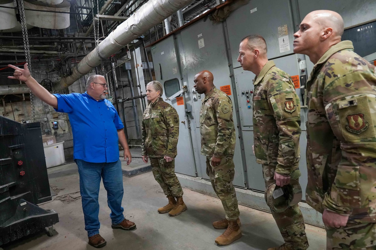 Photo shows people looking at machinery inside a plant.