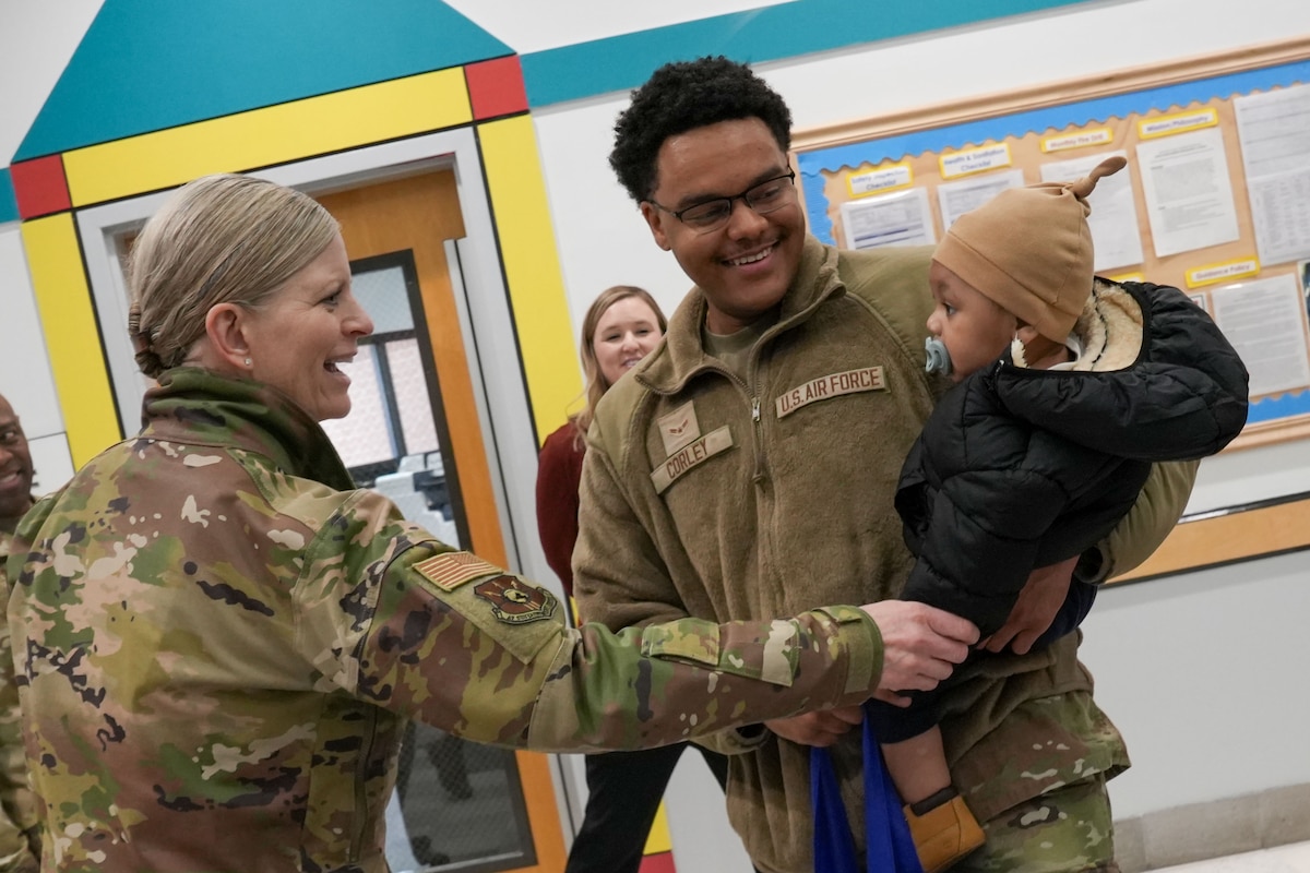 Photo shows two uniformed people smiling and speaking with small child.