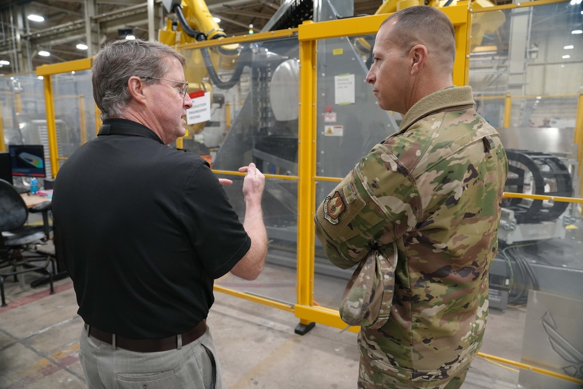 Photo shows two mean speaking in front of large equipment.