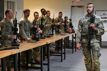 a man stands in front of a classroom and talks about handling a rifle safely