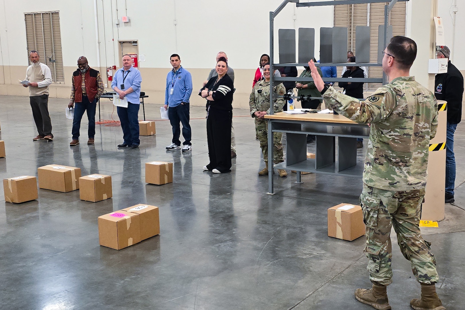 A large group of people stand around a large warehouse looking at one person who is speaking to the group.
