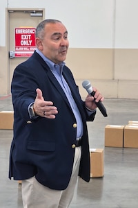 A man stands inside a large warehouse speaking into a microphone.