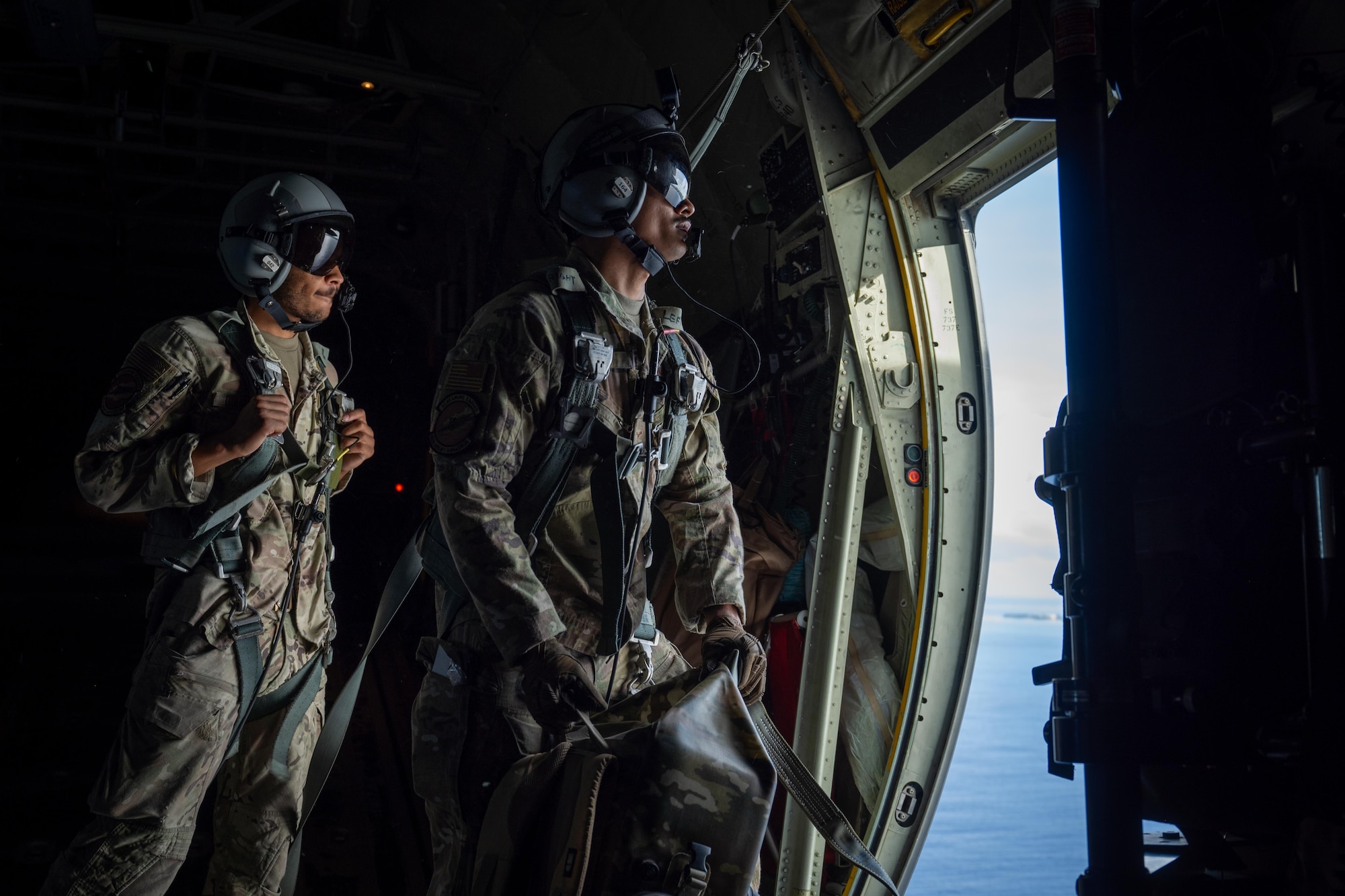 U.S. Air Force Senior Airman Carson Douglas, left, and Airman 1st Class David Wiley, right, loadmasters assigned to the 40th Airlift Squadron, look out a paratroop door aboard a C-130J Super Hercules during Exercise Palmetto Reach near Saipan, Northern Mariana Islands, Jan. 19, 2026. The exercise reinforced the 317th Airlift Wing's role in maintaining a ready, responsive airlift force capable of delivering effects at the speed and scale required in today’s strategic environment. (U.S. Air Force photo by Airman 1st Class Adrien Tran)