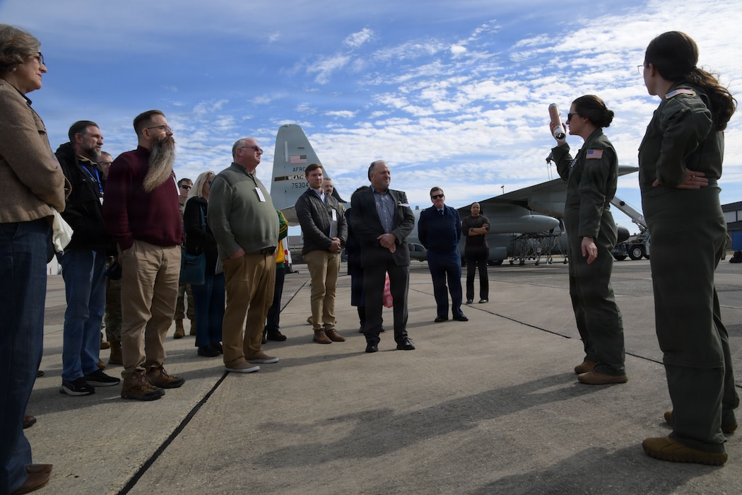 Two military members speak to a group of people in front of a C-130 aircraft.