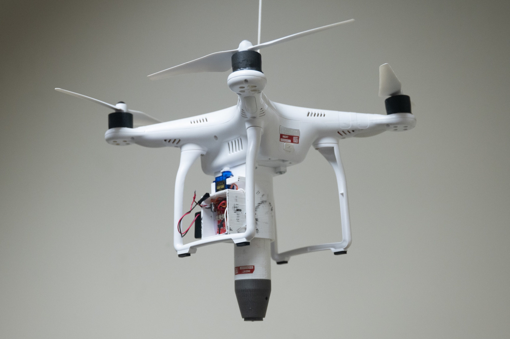 A quadcopter drone equipped with a payload carrier is suspended from the ceiling in a classroom at Joint Base Elmendorf-Richardson, Alaska, Jan. 28, 2026. Even small drone models can carry payloads up to two pounds, including potentially explosive materials. (U.S. Air Force photo by Airman 1st Class Theodore Gowdy)