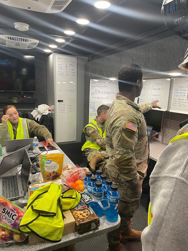Soldiers look at white boards inside a tactical operations vehicle.