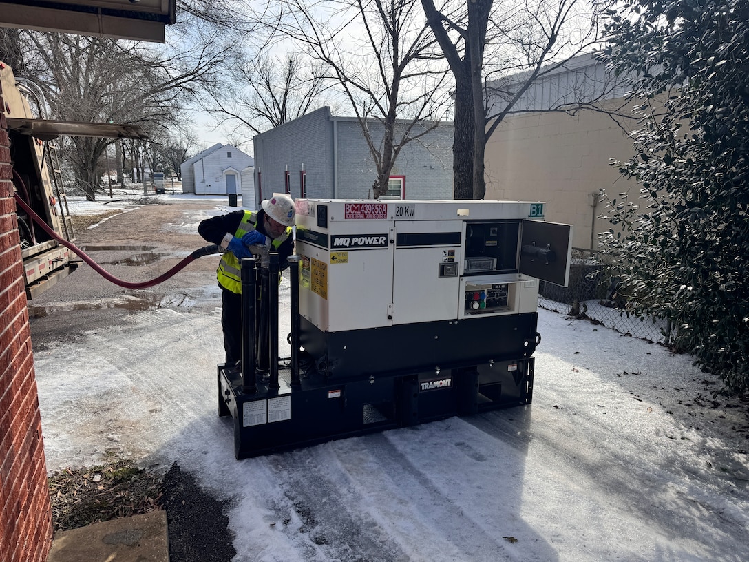 a man uses a fuel line to fill up the gas tank of a large generator.
