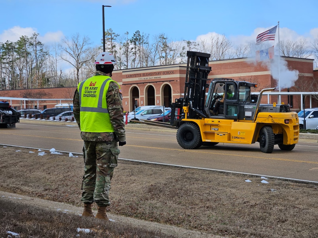 a Soldier watches as a forklift drives down the road past him.