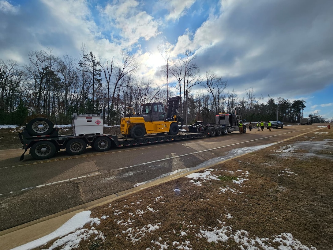 a forklift and an external fuel tank for a generator are on a large flatbed trailer in the middle of a roadway.