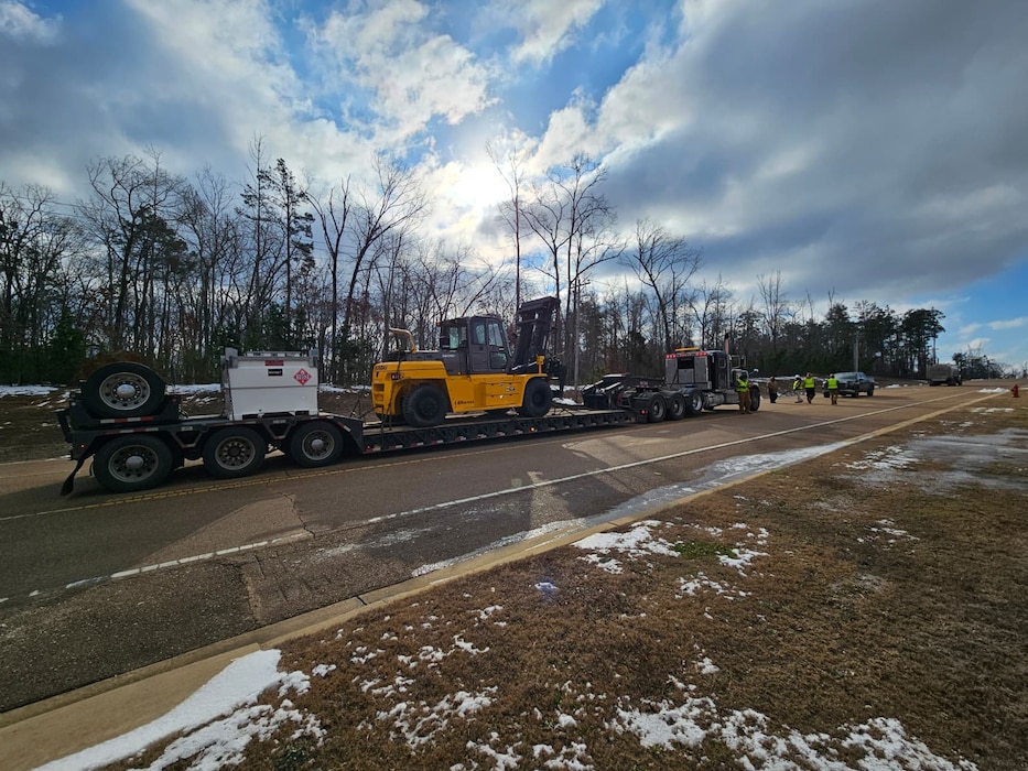 a forklift and an external fuel tank for a generator are on a large flatbed trailer in the middle of a roadway.