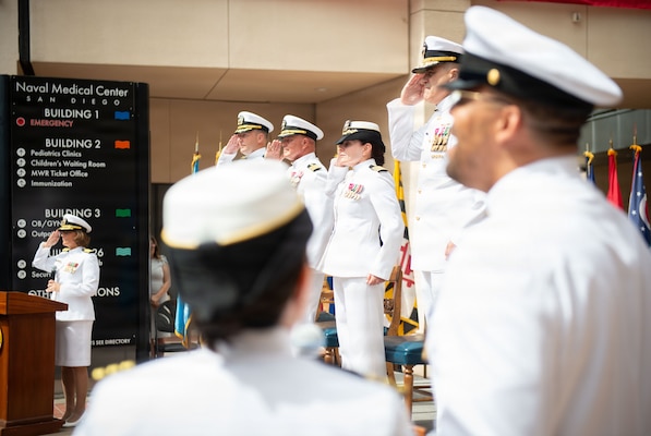 The official party for the Navy Medicine Readiness and Training Command (NMRTC) San Diego change of command and Naval Medical Center San Diego (NMCSD) transfer of directorship ceremony renders honors during the parading of the colors and singing of the National Anthem at NMCSD, June 30, 2026. NMRTC San Diego supports Navy and Marine Corps readiness by ensuring its medical forces are ready to deploy and provide medical support, ashore or at sea. The mission of NMCSD is to optimize health and enhance readiness. NMCSD employs more than 5,500 active-duty military personnel, civilians, and contractors in southern California to deliver exceptional care afloat and ashore. (U.S. Navy photo by Mass Communication Specialist 1st Class Marcus Stanley)