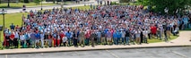 A large group of people predominantly wearing red, white, and blue pose for a photo on a lawn area.