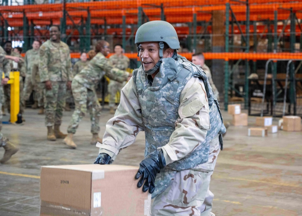Airman in gear pushes a box for a relay race.