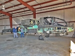 Two workers examine a partially deconstructed Apache attack helicopter in a hangar.