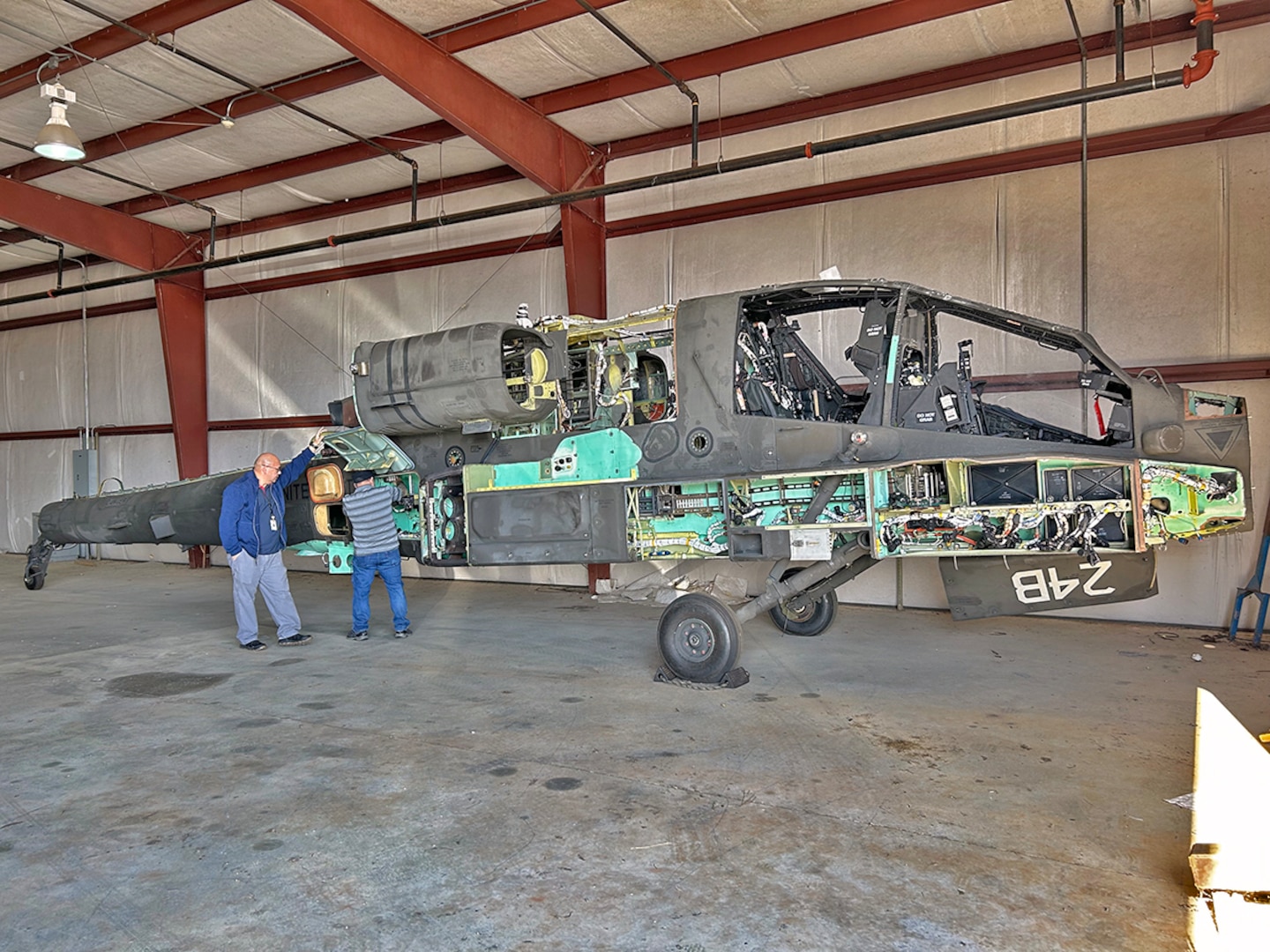 Two workers examine a partially deconstructed Apache attack helicopter in a hangar.
