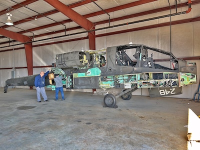 Two workers examine a partially deconstructed Apache attack helicopter in a hangar.
