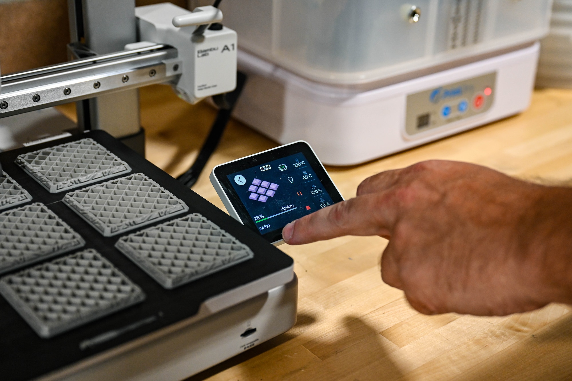 A hand touches a 3D printing machine screen.