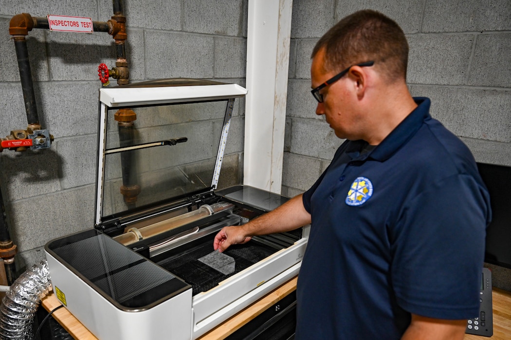 A man stands at an engraving machine and reach down to place a piece of material into it.