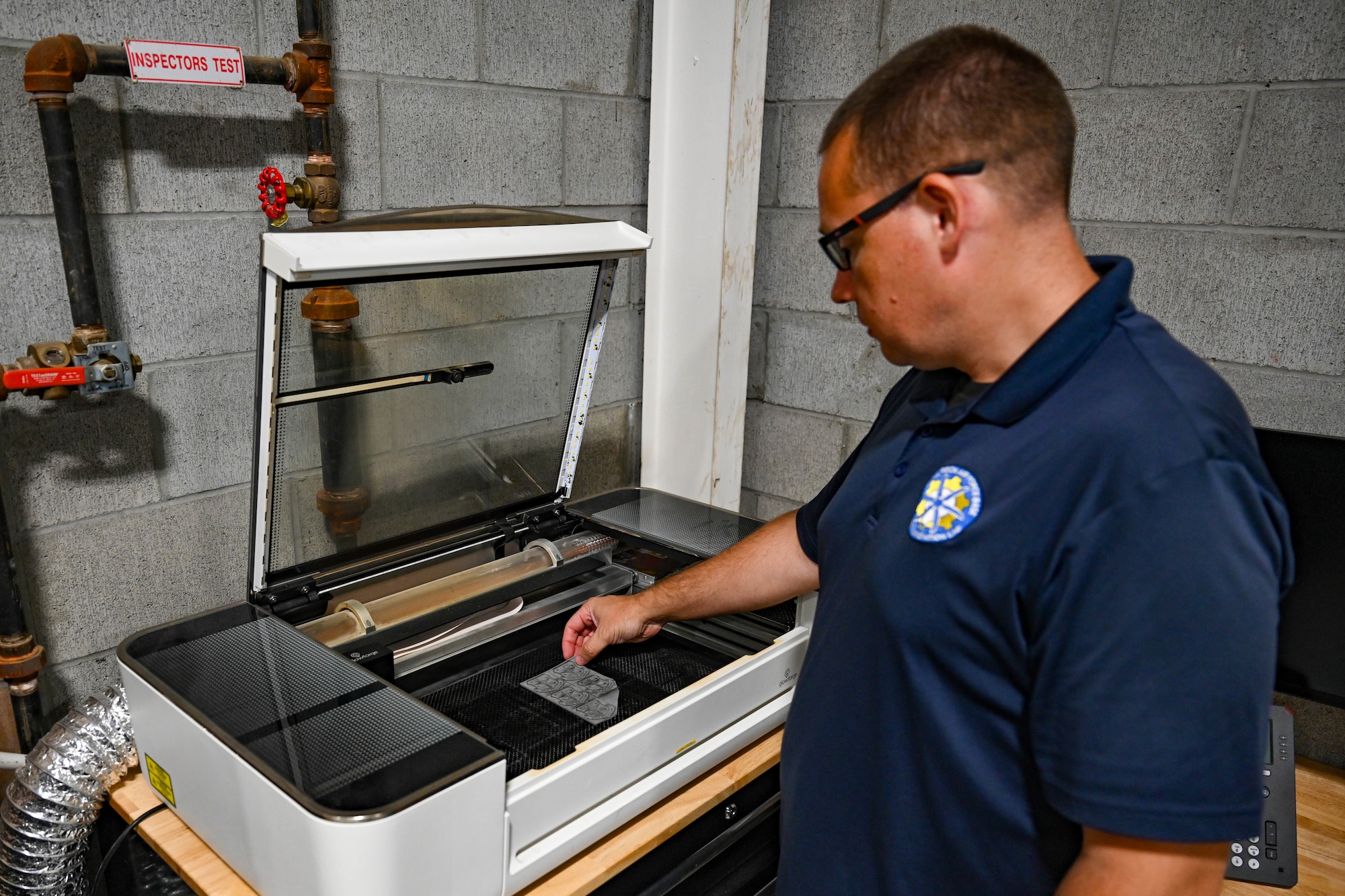 A man stands at an engraving machine and reach down to place a piece of material into it.