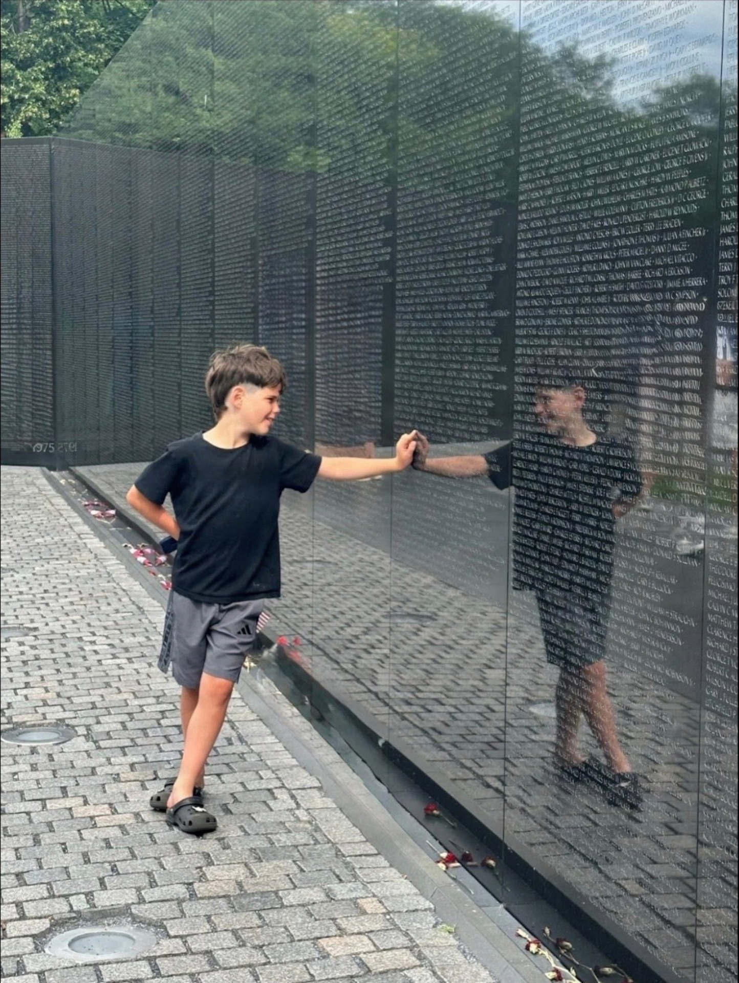 Eight-year-old Fynn Williams reaches out to touch the reflective black granite surface of the Vietnam Veterans Memorial Wall in Washington, D.C.