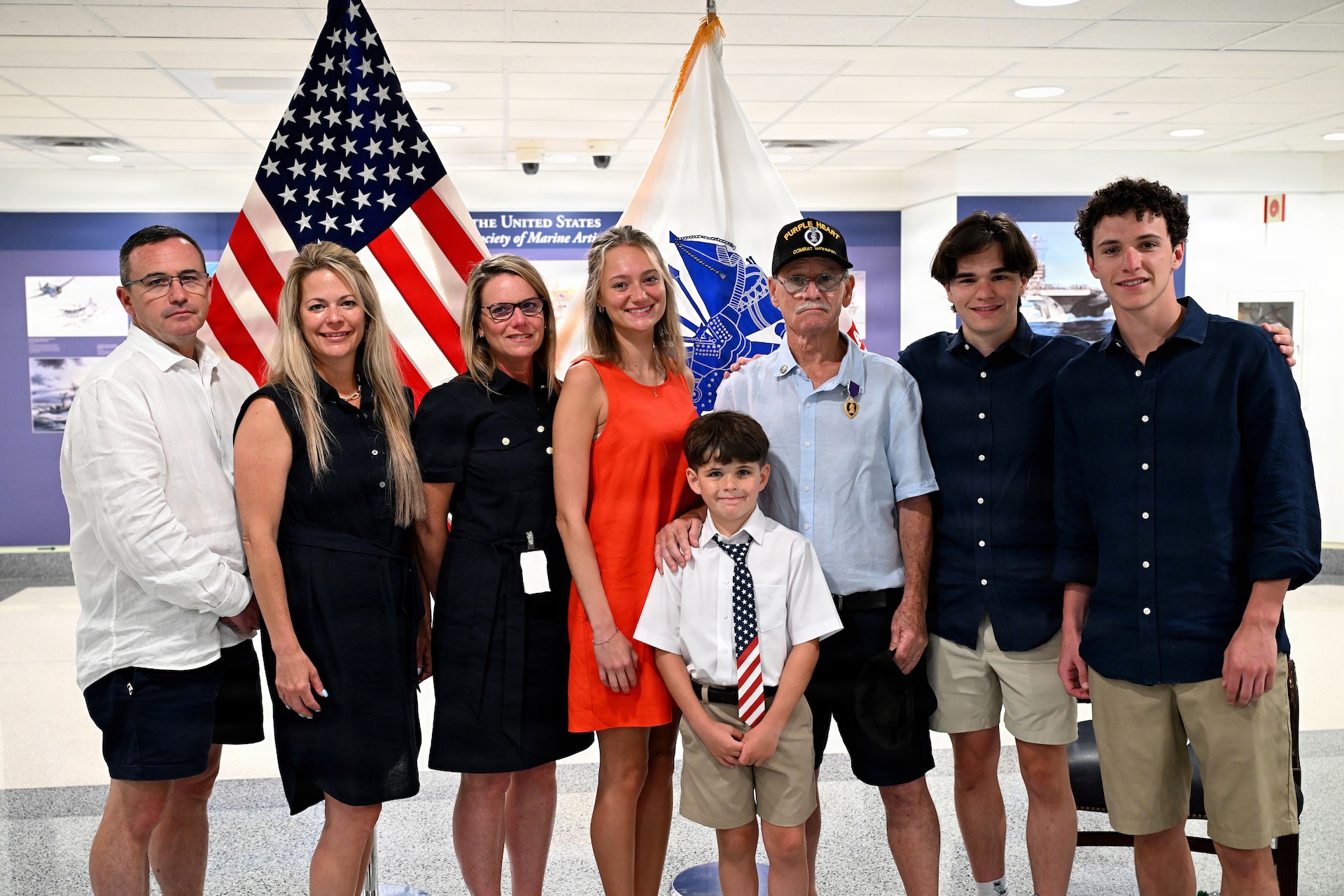 A group photograph from a Purple Heart ceremony at the Pentagon. Specialist Fourth Class Raymond Steven Williams stands in the center, surrounded by his smiling family. From left to right are his son Eric, daughter-in-law Jennifer, daughter Kelly, granddaughter Krysta, grandson Fynn, Williams himself, and grandsons Blake and Cohen.