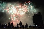Silhouettes of audience members watching white and red fireworks