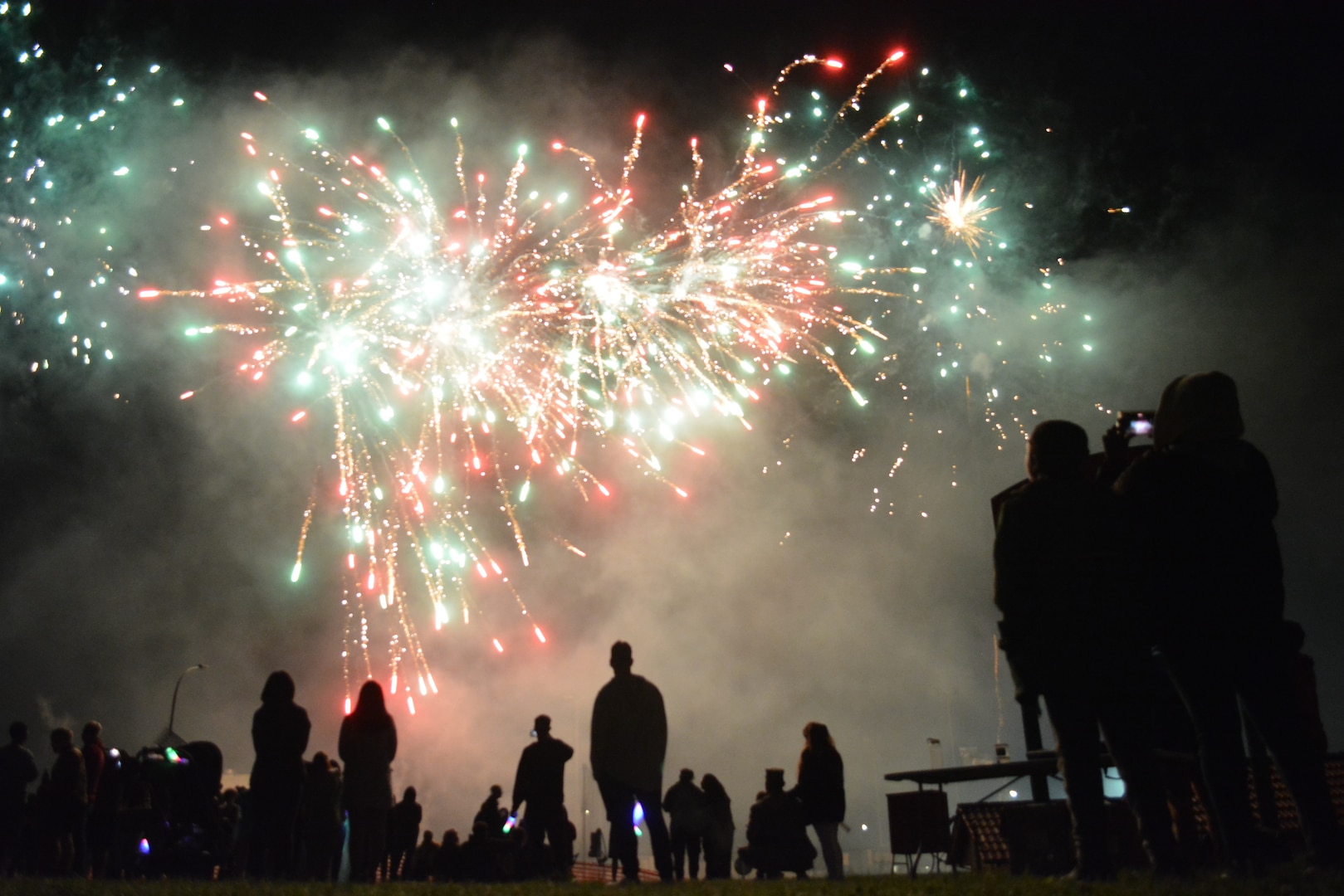 Silhouettes of audience members watching white and red fireworks